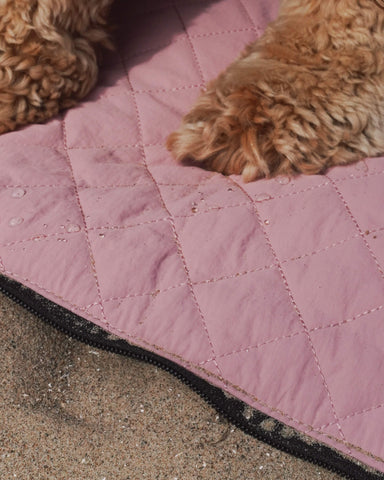 Close-up of waterproof dusty pink dog travel bed fabric with water droplets and dog paws – foldable dog mat by BONES